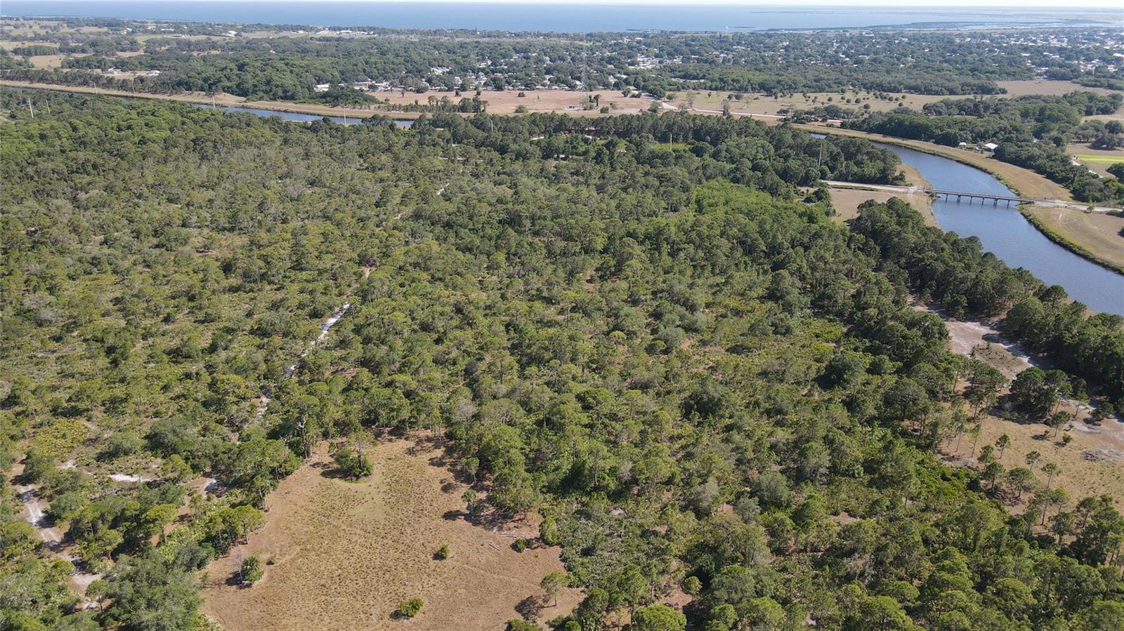 An aerial view shows a large, wooded lot bordering a river with a bridge nearby — 4340 Highway 710, Okeechobee FL 34974, OKEECHOBEE, FL