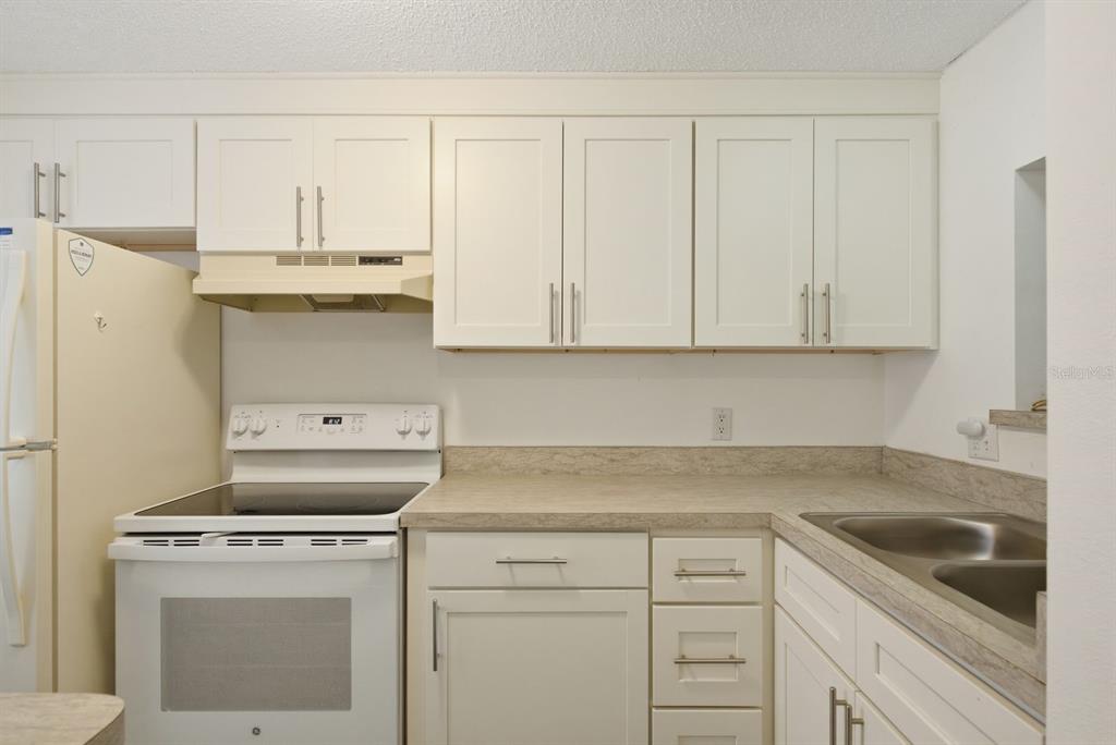 A kitchen features white cabinets, a white stove, and a beige laminate countertop — 3309 TROPHY BOULEVARD, NEW PORT RICHEY, FL