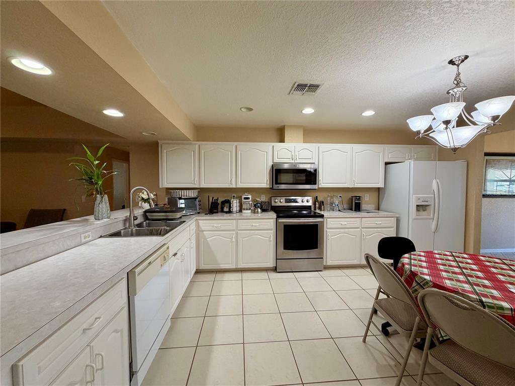 A kitchen with white cabinets, stainless steel appliances, tile flooring, and a dining table — 1762 GREY FOX DRIVE, LAKELAND, FL