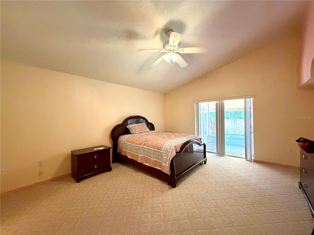 A bedroom with beige carpet, a dark wood bed frame, and sliding glass patio doors — 1762 GREY FOX DRIVE, LAKELAND, FL