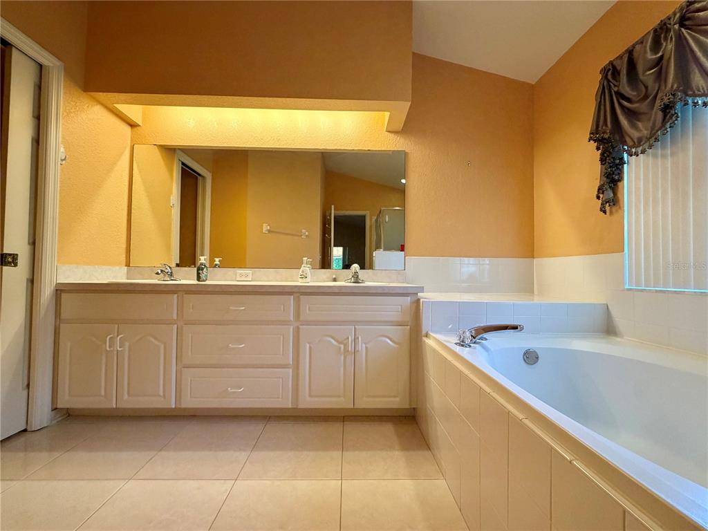 A bathroom features a double vanity with white cabinets, a large mirror, and a soaking tub — 1762 GREY FOX DRIVE, LAKELAND, FL