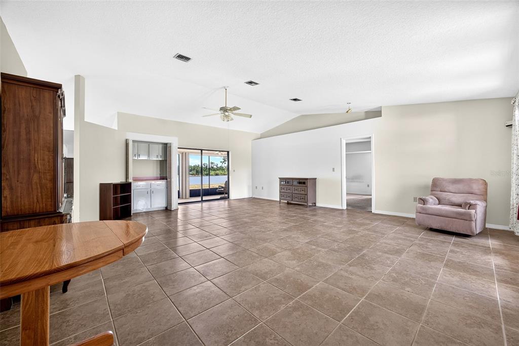 A spacious living room features light-colored walls, tile flooring, a vaulted ceiling, and sliding glass doors — 25192 DERRINGER ROAD, PUNTA GORDA, FL