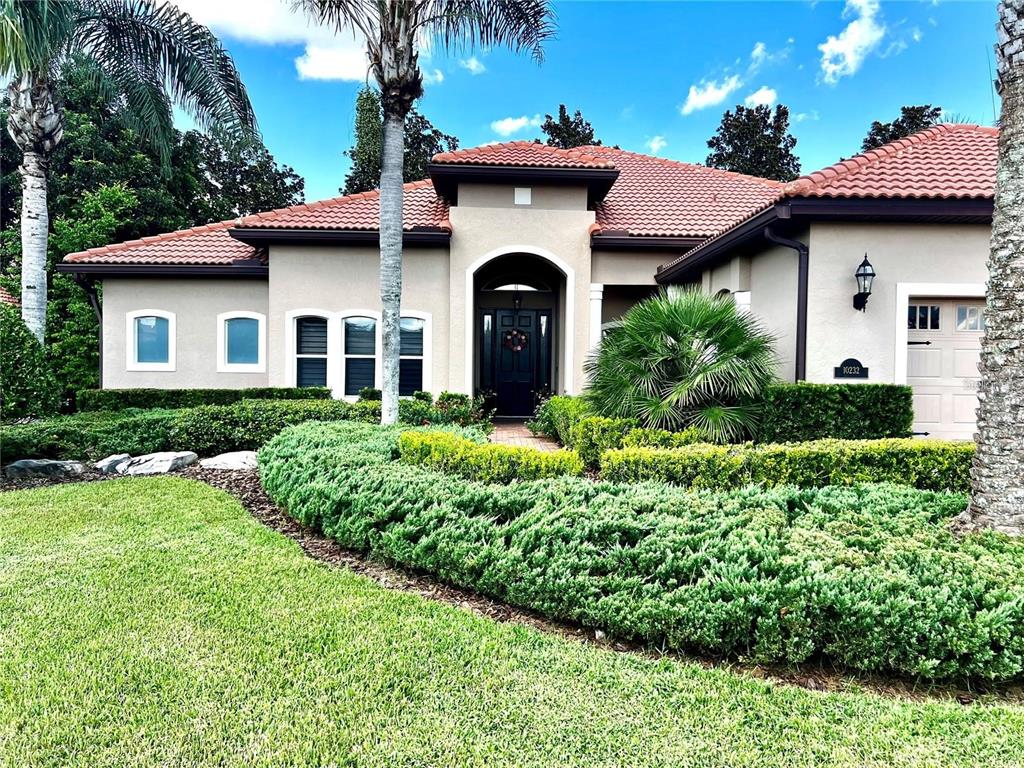 A single-story house with a tiled roof, arched entryway, and manicured landscaping in the front yard — 10232 YONAOMI CIRCLE, CLERMONT, FL