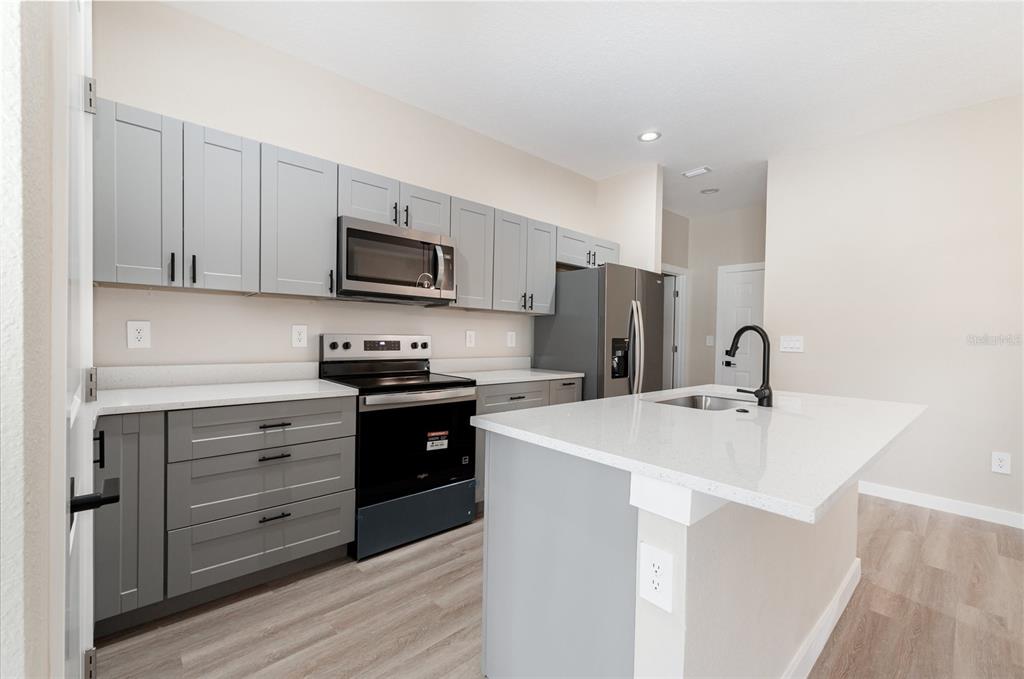 A modern kitchen features gray cabinets, stainless steel appliances, and a white quartz island countertop — 15615 SW 49TH AVENUE ROAD, OCALA, FL