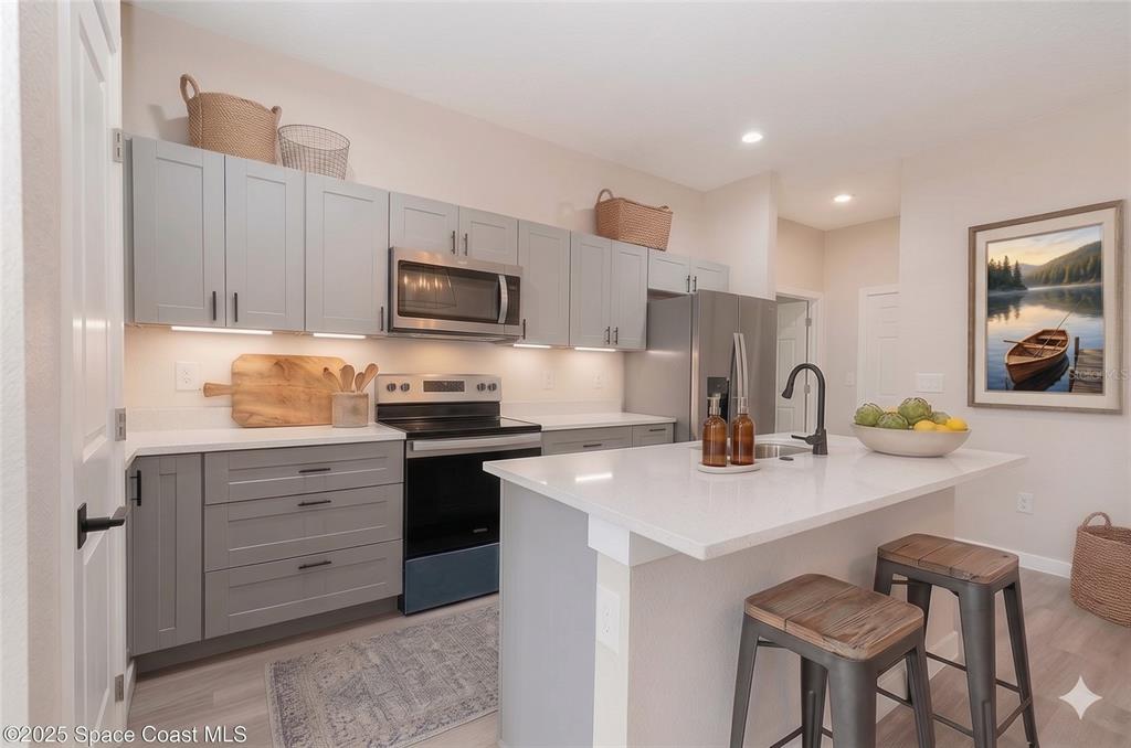 A modern kitchen features gray cabinets, stainless steel appliances, a white island, and bar stools — 15615 SW 49TH AVENUE ROAD, OCALA, FL
