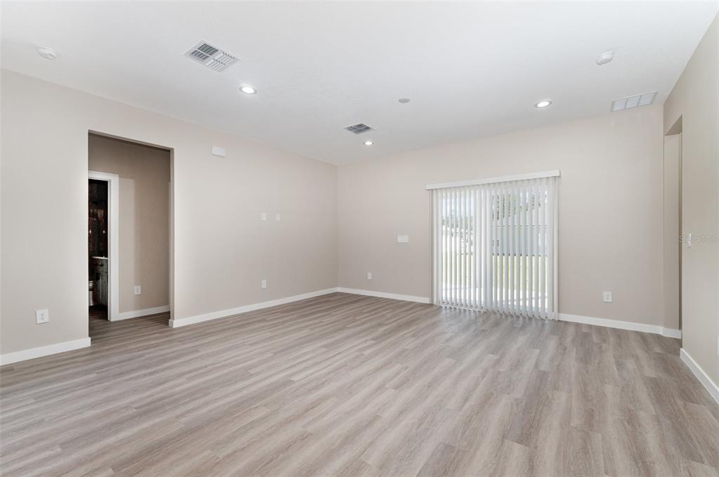 An empty living room features light-colored walls, wood-look flooring, recessed lighting, and sliding glass doors — 15615 SW 49TH AVENUE ROAD, OCALA, FL