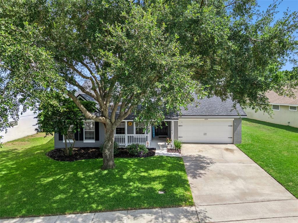 A single-story house with a white garage, a front porch, and a large tree — 1094 GOLF POINT LOOP, APOPKA, FL