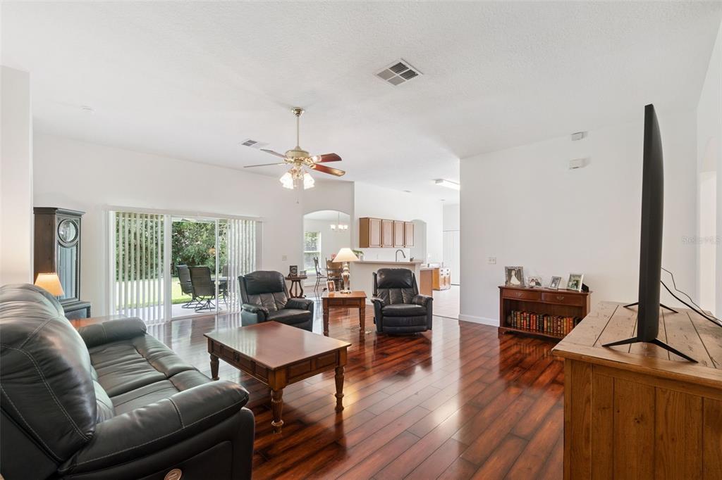 A living room with dark wood flooring, leather furniture, a ceiling fan, and sliding glass doors — 1094 GOLF POINT LOOP, APOPKA, FL