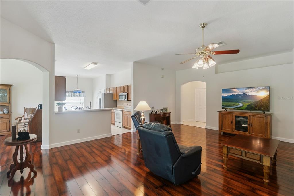 A living room with dark wood floors, a ceiling fan, and an open kitchen view — 1094 GOLF POINT LOOP, APOPKA, FL
