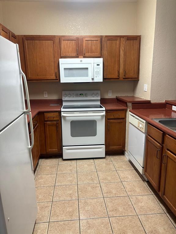 A kitchen features wood cabinets, white appliances, and a tiled floor — 8103 LILLIES WAY UNIT 107, ORLANDO, FL