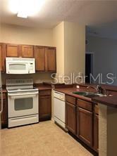 A kitchen features wood cabinets, white appliances, and a sink with a breakfast bar — 8103 LILLIES WAY UNIT 107, ORLANDO, FL