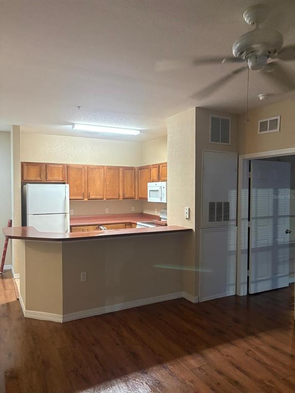 A kitchen features wood cabinets, white appliances, a breakfast bar, and wood-look flooring — 8103 LILLIES WAY UNIT 107, ORLANDO, FL