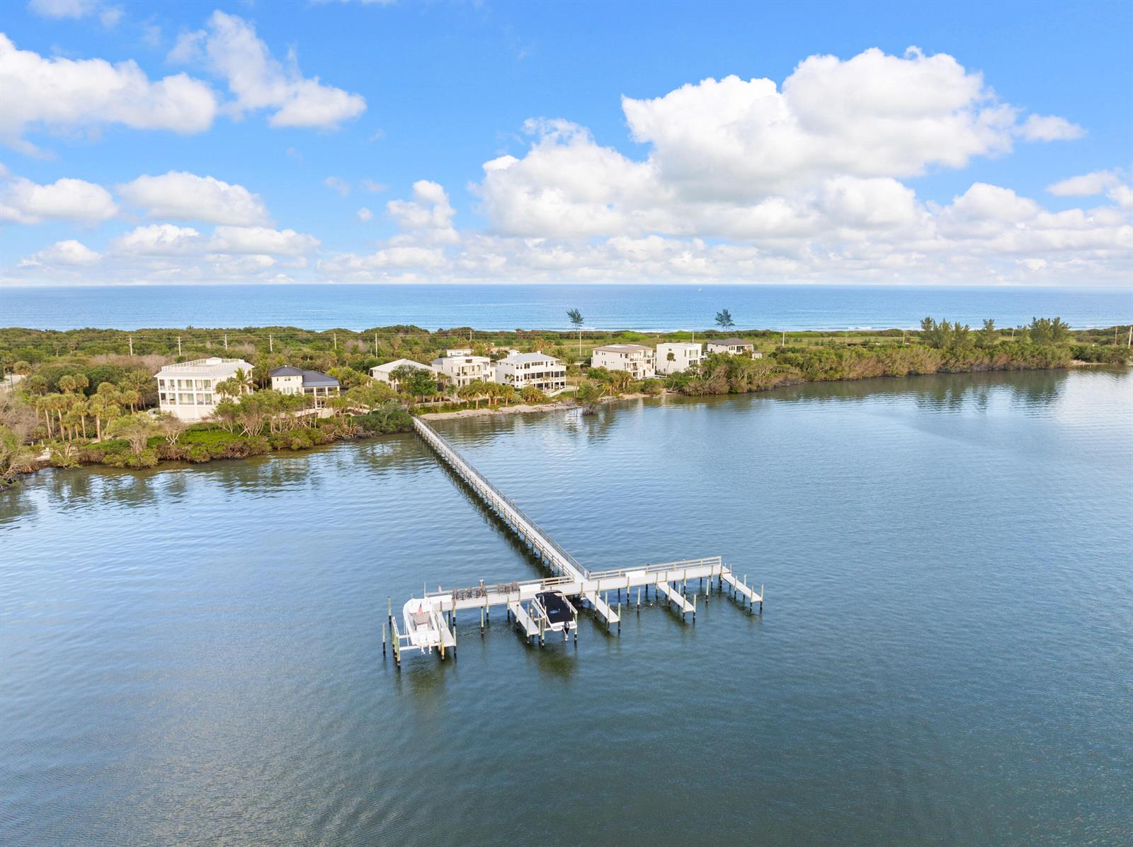An aerial view shows a long wooden dock extending into a bay near coastal houses — 7671 Pelican Pointe Drive, Jensen Beach FL 34957, JENSEN BEACH, FL