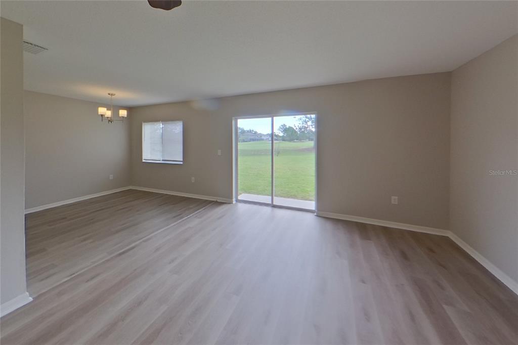 An empty living room features light wood-look flooring, neutral walls, and a sliding glass door — 13130 FENNWAY RIDGE DRIVE, RIVERVIEW, FL