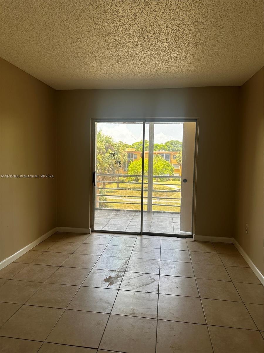 An empty room features beige tiled floors, tan walls, and a sliding glass door to a balcony — 4324 NW 9th Ave # 3A, Deerfield Beach FL 33064, DEERFIELD BEACH, FL