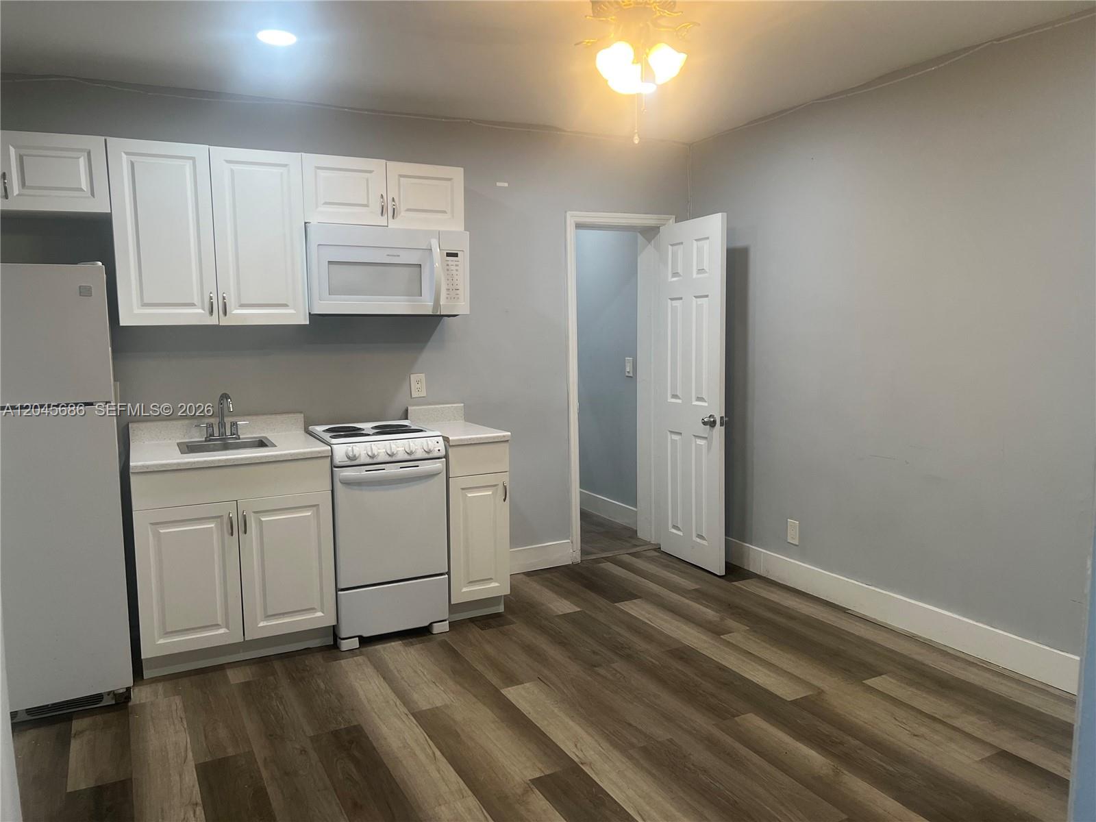 A small kitchen features white cabinets, a white stove, and wood-look flooring — 2118 N 19th Ave # 4, Hollywood FL 33020, HOLLYWOOD, FL