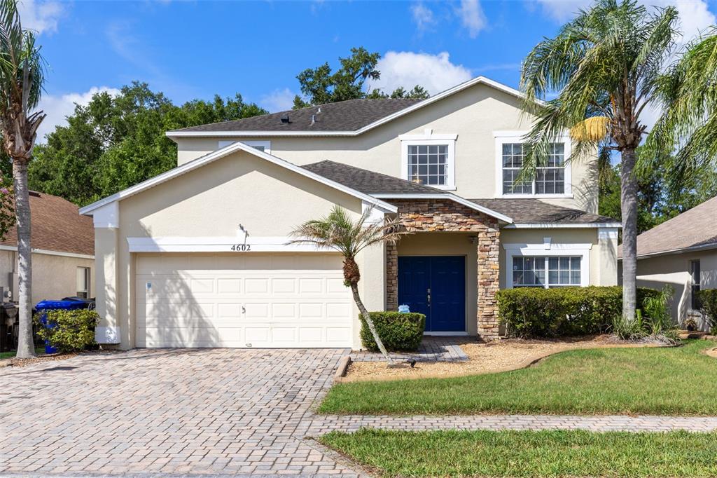 A two-story suburban house with a beige stucco exterior, stone accents, and a paved driveway — 4602 CUMBRIAN LAKES DRIVE, KISSIMMEE, FL