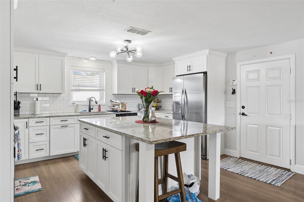 A white kitchen features a granite-topped island, stainless steel appliances, and wood-look flooring — 273 AVALON ROAD, WINTER GARDEN, FL