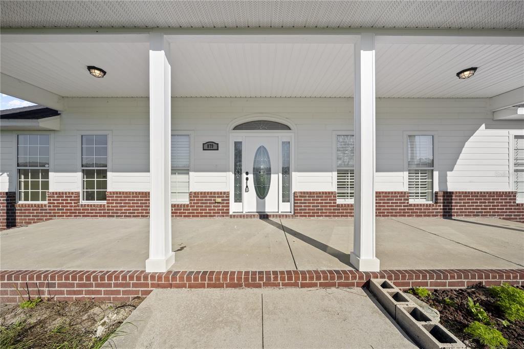 A white house exterior features a covered front porch with brick accents and columns — 879 NW MILO TERRACE, LAKE CITY, FL
