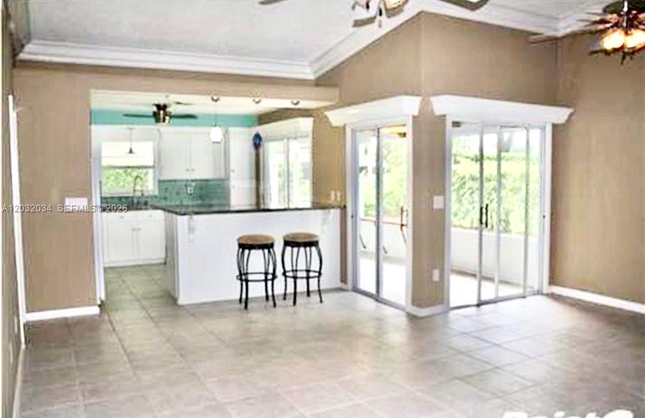 An open-concept kitchen with a breakfast bar overlooks a tiled living area with sliding doors — 600 SE 19th Dr, Homestead FL 33033, HOMESTEAD, FL
