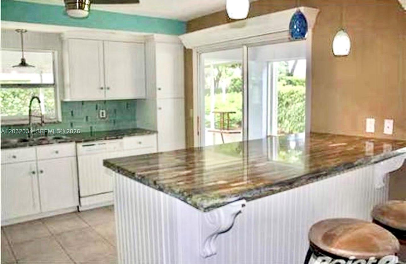 A kitchen features white cabinetry, a stone-topped island, and a sliding glass door — 600 SE 19th Dr, Homestead FL 33033, HOMESTEAD, FL