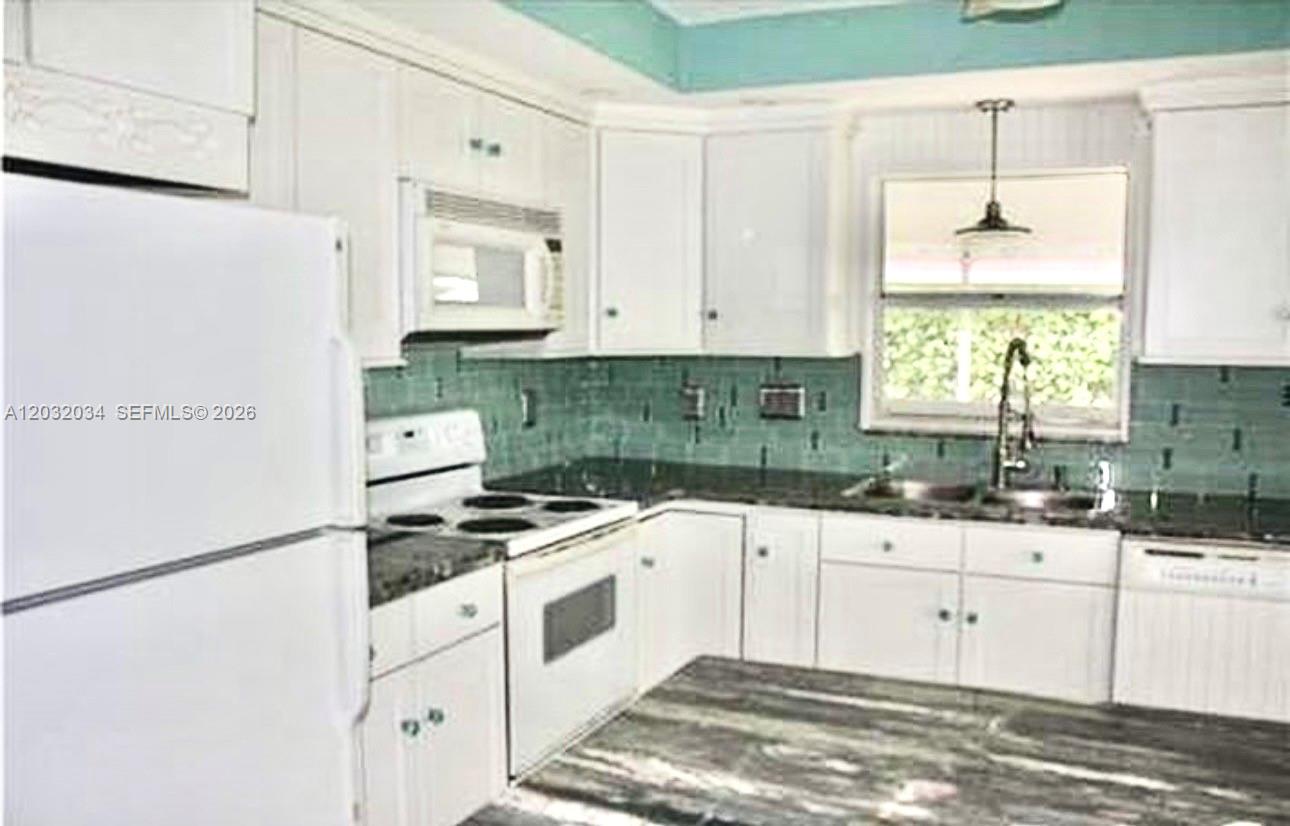 A kitchen features white cabinets, a dark countertop, a teal backsplash, and white appliances — 600 SE 19th Dr, Homestead FL 33033, HOMESTEAD, FL