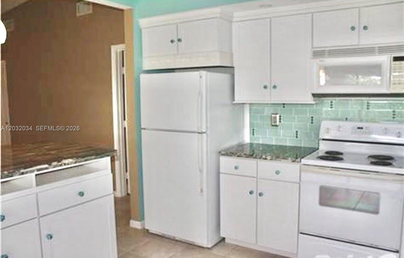 A kitchen features white cabinets, a white refrigerator, a white stove, and light green backsplash tiles — 600 SE 19th Dr, Homestead FL 33033, HOMESTEAD, FL