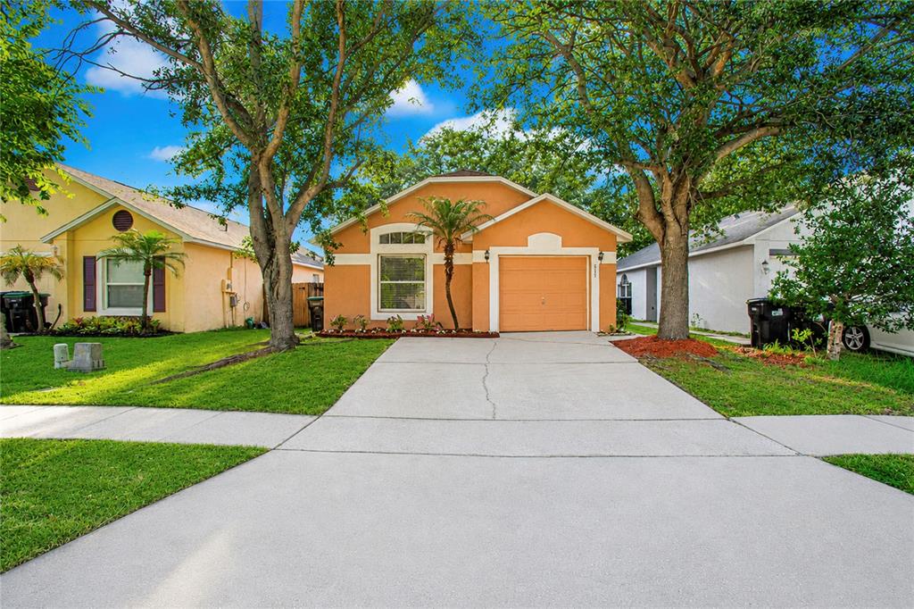 A single-story orange house with a concrete driveway and two large trees in the front — 519 BEASLEY COURT, ORLANDO, FL