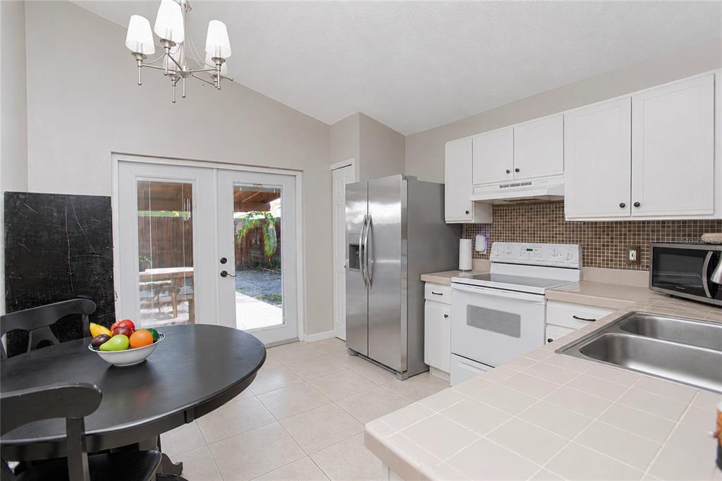 A kitchen with white cabinets, stainless steel refrigerator, tile countertops, and a dining area — 519 BEASLEY COURT, ORLANDO, FL