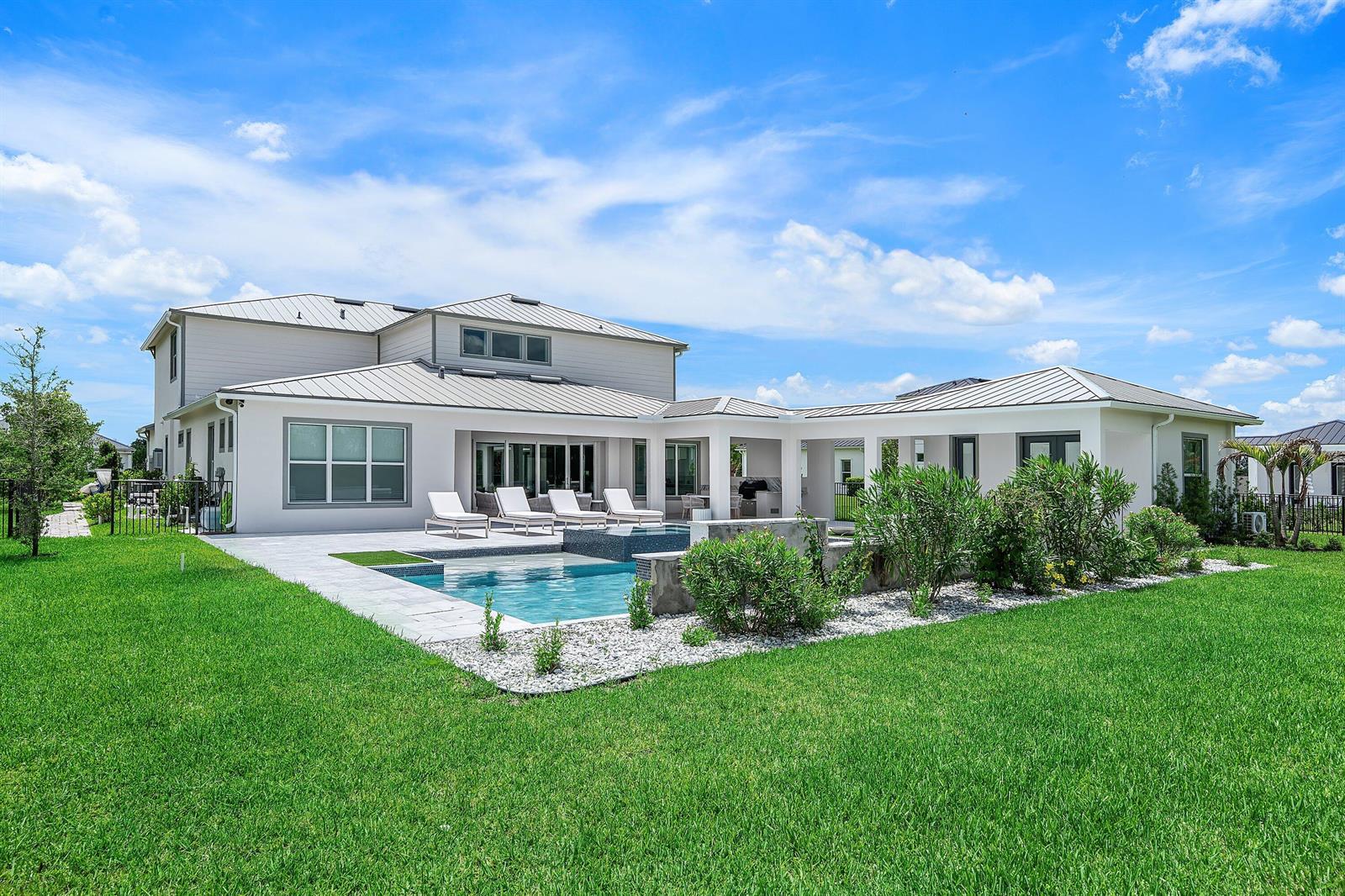 A two-story house with a backyard swimming pool, patio, and landscaped garden under a blue sky — 20020 SE Bridgewater Drive, Jupiter FL 33458, JUPITER, FL