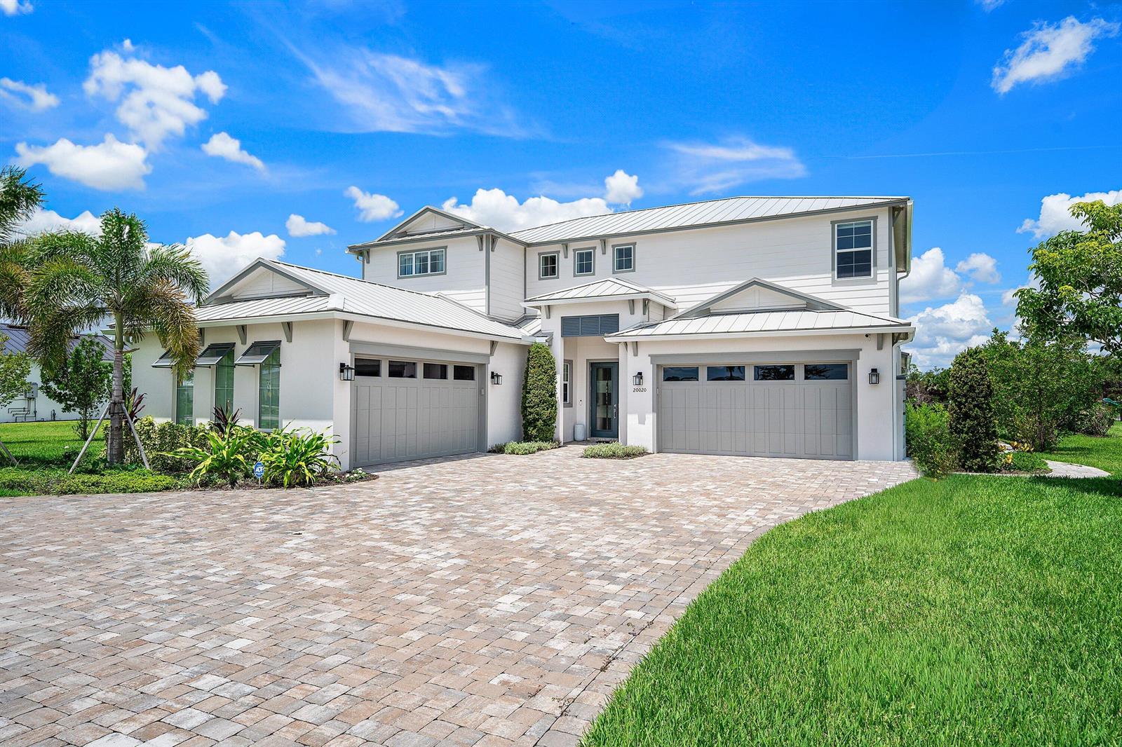 A two-story house with a metal roof, gray garage doors, and a paved driveway — 20020 SE Bridgewater Drive, Jupiter FL 33458, JUPITER, FL