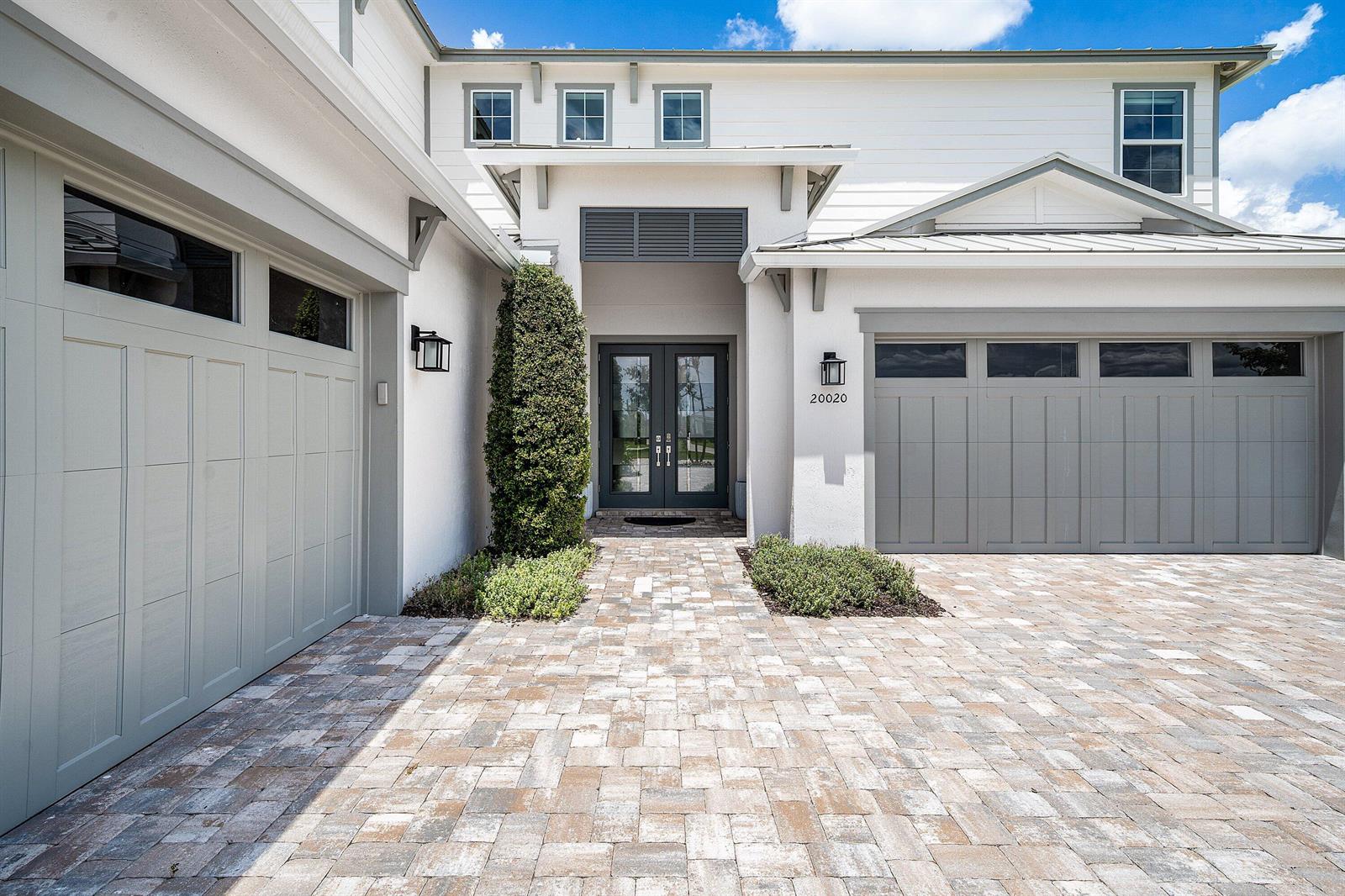 A white two-story house features a paver driveway, two garage doors, and a double-door entrance — 20020 SE Bridgewater Drive, Jupiter FL 33458, JUPITER, FL