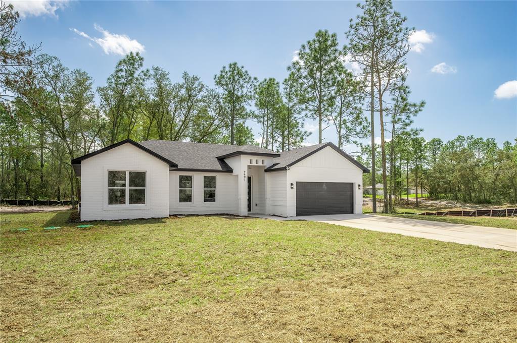 A white, single-story house with a black garage door and roof sits on a lawn — 9609 N VAUGHN DRIVE, CITRUS SPRINGS, FL