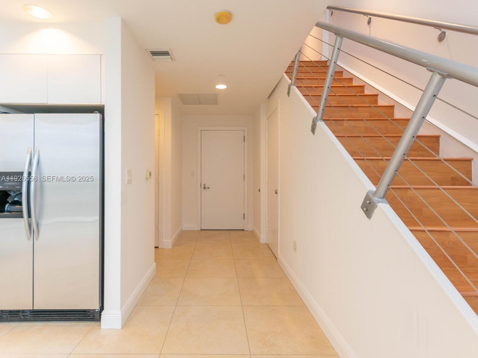 A hallway features beige tile flooring, a stainless steel refrigerator, and a wooden staircase — 1050 Brickell Ave # 606, Miami FL 33131, MIAMI, FL