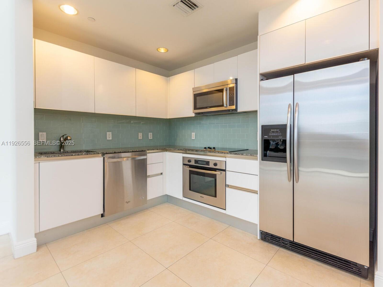 A modern kitchen features white cabinetry, stainless steel appliances, and a light green tiled backsplash — 1050 Brickell Ave # 606, Miami FL 33131, MIAMI, FL