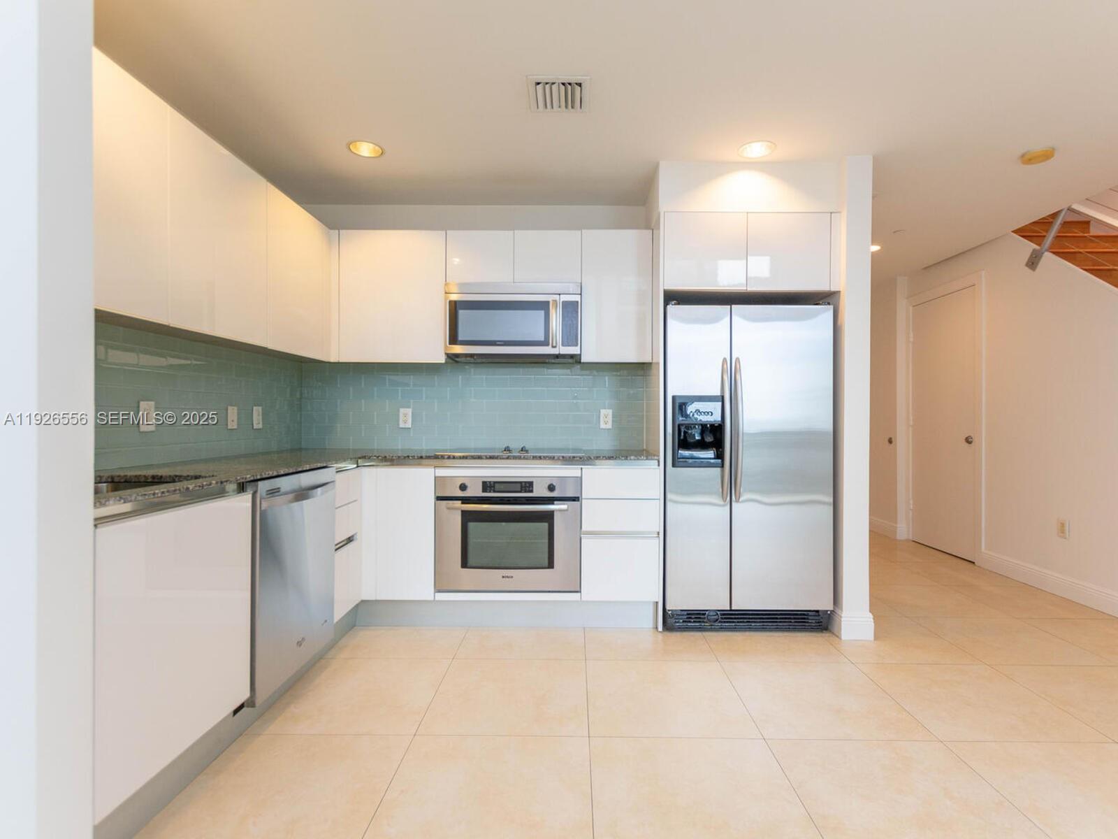 A modern kitchen features white cabinets, stainless steel appliances, and a light green tile backsplash — 1050 Brickell Ave # 606, Miami FL 33131, MIAMI, FL