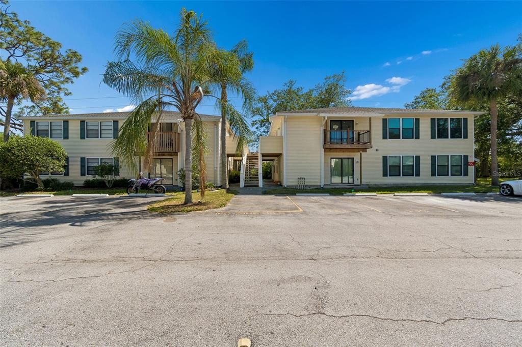 An exterior view of a two-story apartment building with yellow siding and a parking lot — 140 HUNTER LAKE DRIVE UNIT 8C, OLDSMAR, FL