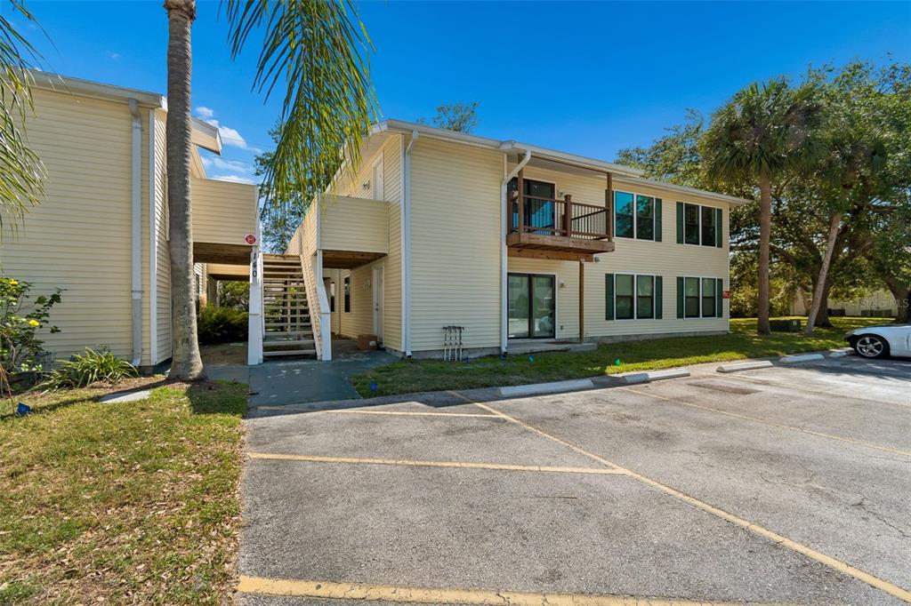 Exterior view of a two-story apartment building with yellow siding, a wooden balcony, and stairs — 140 HUNTER LAKE DRIVE UNIT 8C, OLDSMAR, FL