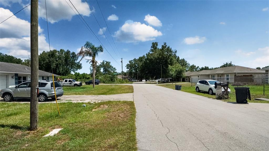 A street view showing houses, parked cars, a utility pole, and a palm tree — 24 PECAN COURSE LOOP, OCALA, FL