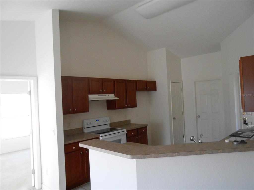 A kitchen features dark wood cabinets, laminate countertops, white appliances, and a vaulted ceiling — 1871 CALAHAN AVENUE, NORTH PORT, FL