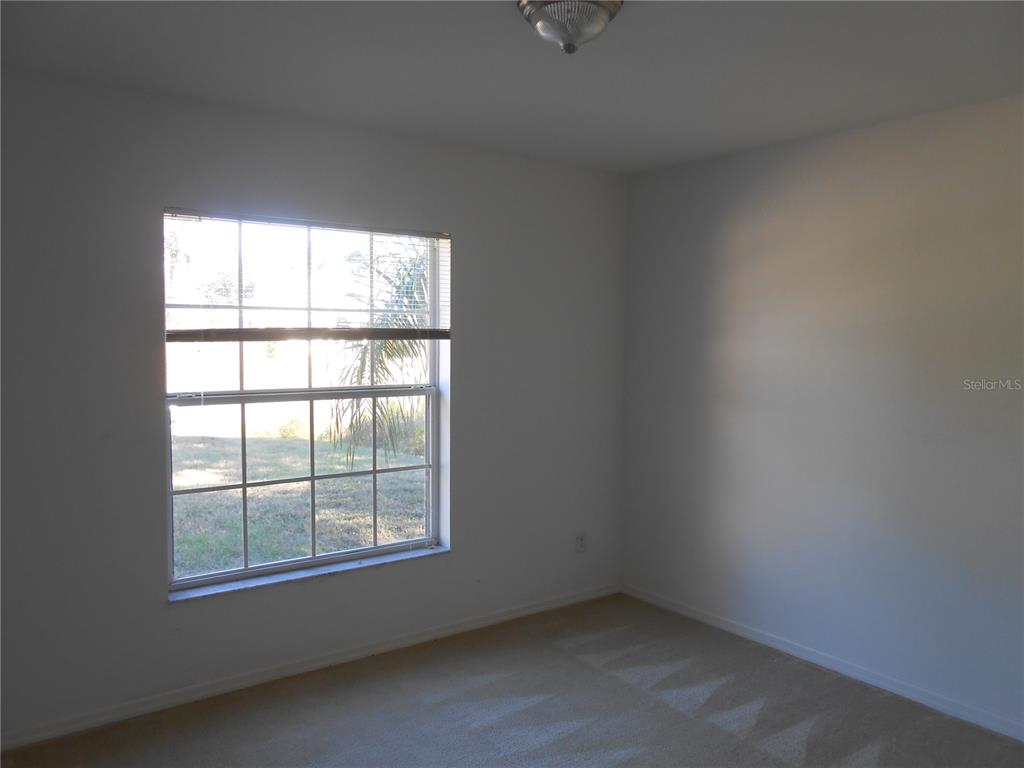 An empty bedroom features white walls, beige carpeting, and a window with blinds — 1871 CALAHAN AVENUE, NORTH PORT, FL