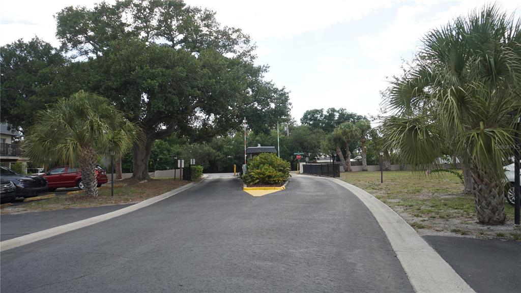 A paved driveway leads to a gated entrance with a guard booth and palm trees — 3312 RAMBLEWOOD PLACE, SARASOTA, FL