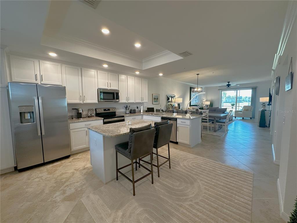 A kitchen with white cabinets, granite countertops, and an island opens into a living area — 14040 HERITAGE LANDING BOULEVARD UNIT 116, PUNTA GORDA, FL