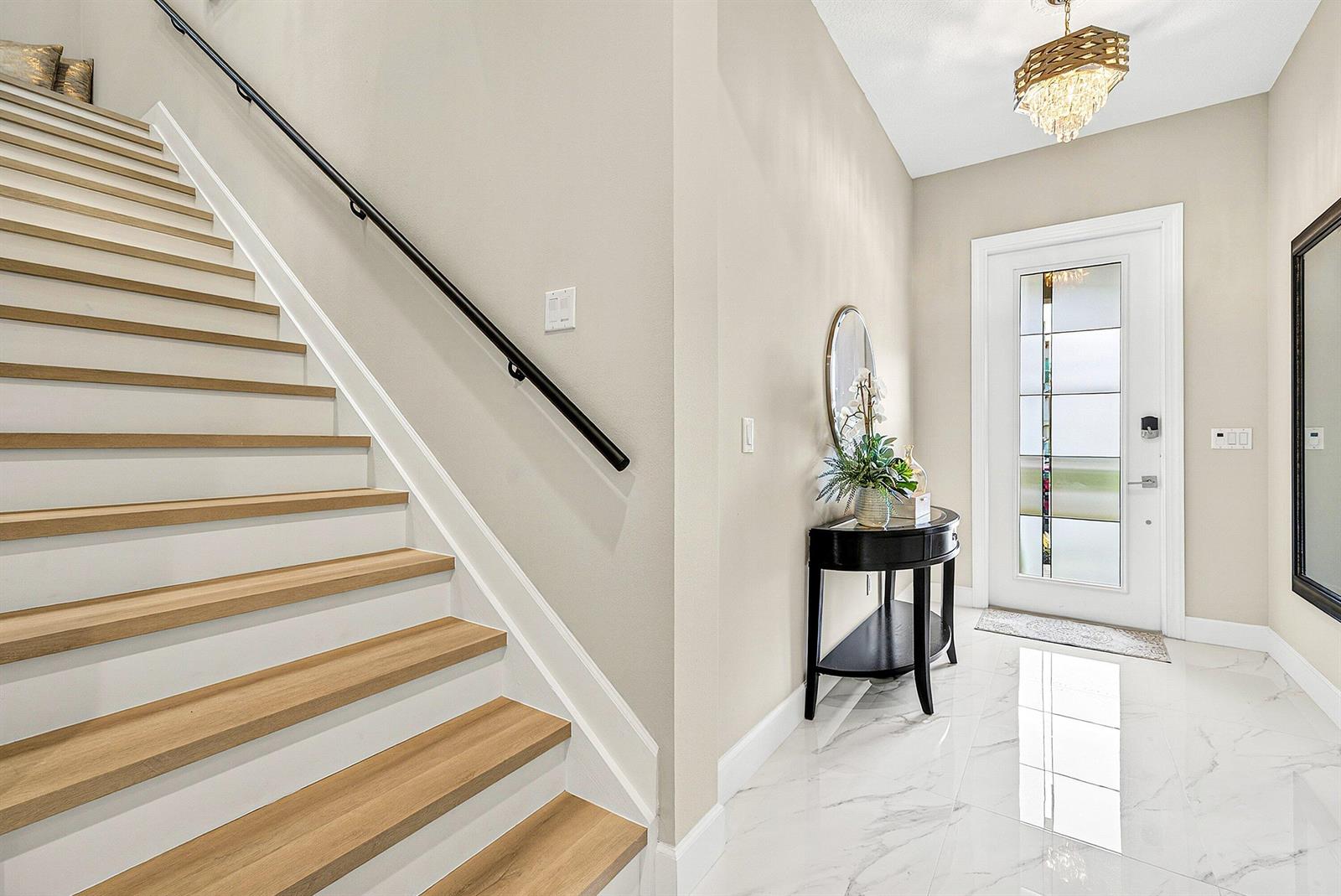 A bright entryway features a staircase with wood treads, marble-look tile flooring, and a chandelier — 4767 Marston Lane, Lake Worth FL 33467, LAKE WORTH, FL
