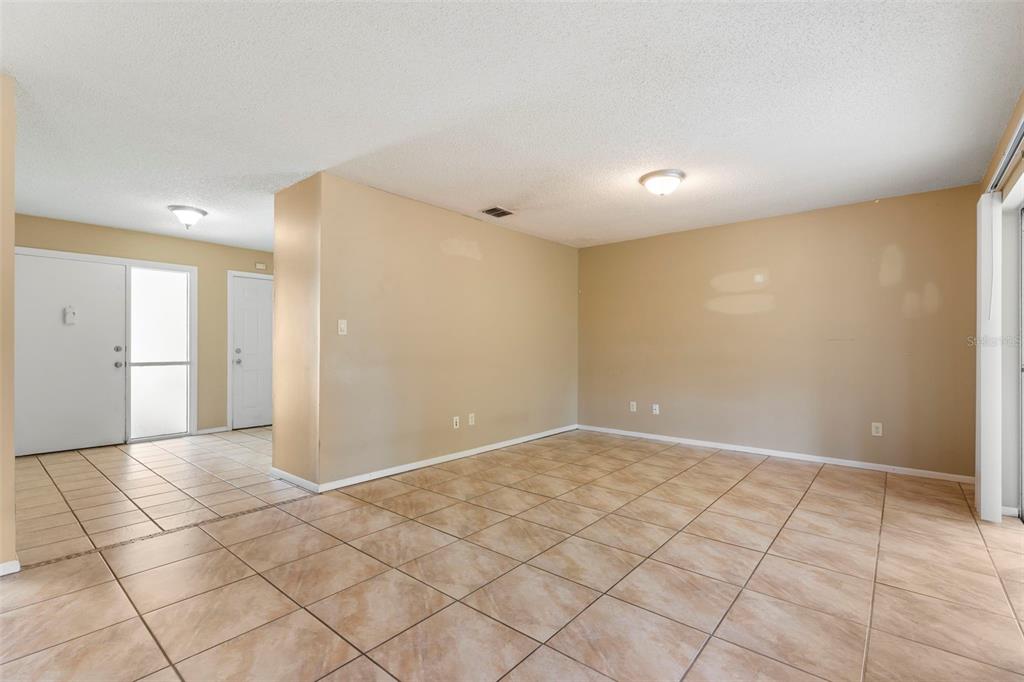 An empty room with beige walls and light-colored tiled flooring featuring a sliding glass door — 10312 LAZY LAKE DRIVE, ORLANDO, FL