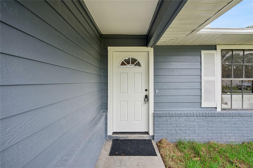 A white front door with a semi-circular window is set in a gray-painted exterior wall — 1110 CATHERINE STREET, ORANGE CITY, FL