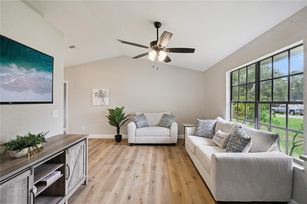A living room features light wood flooring, a vaulted ceiling, a ceiling fan, and large windows — 1110 CATHERINE STREET, ORANGE CITY, FL