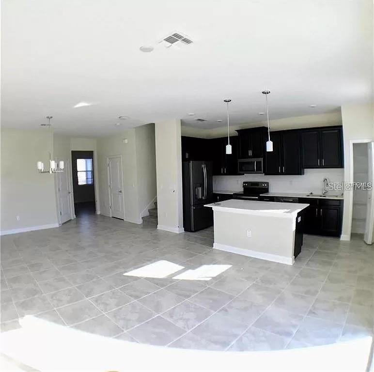 An open-concept kitchen features dark cabinetry, a central island, and light tile flooring — 4652 TRIBUTE TRAIL, KISSIMMEE, FL