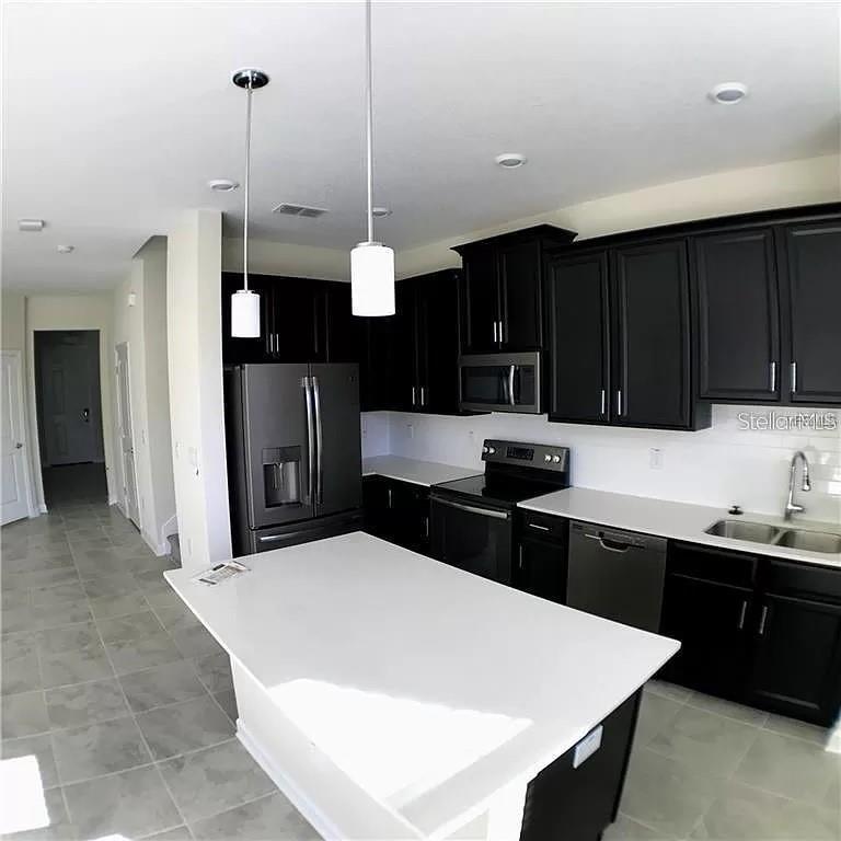 A kitchen features dark cabinetry, white countertops, a central island, and stainless steel appliances — 4652 TRIBUTE TRAIL, KISSIMMEE, FL