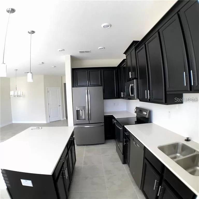 A modern kitchen features dark cabinets, white countertops, stainless steel appliances, and a central island — 4652 TRIBUTE TRAIL, KISSIMMEE, FL